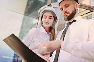 A woman and a man in business clothes and in white construction helmets discuss a construction plan or a contract