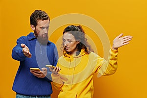 Woman man cheerful couple with phones in hand social networking and communication crooked smile fun and fight, in yellow