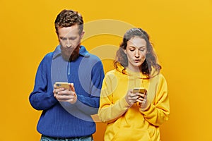 Woman man cheerful couple with phones in hand social networking and communication crooked smile fun and fight, in yellow