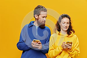 Woman man cheerful couple with phones in hand social networking and communication crooked smile fun and fight, in yellow