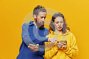 Woman man cheerful couple with phones in hand social networking and communication crooked smile fun and fight, in yellow