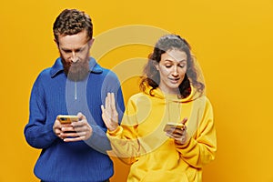 Woman man cheerful couple with phones in hand social networking and communication crooked smile fun and fight, in yellow