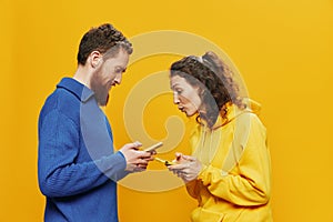 Woman man cheerful couple with phones in hand social networking and communication crooked smile fun and fight, in yellow