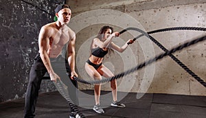 Woman and man couple training together doing battling rope workout