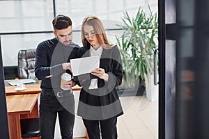 Woman and man in formal clothes with documents talking to each other in the office