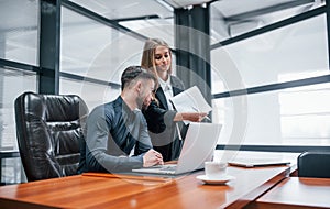 Woman and man in formal clothes working together indoors in the office by table