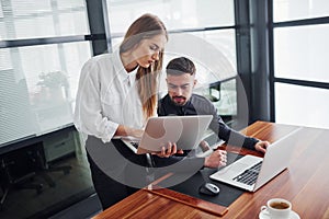 Woman and man in formal clothes working together indoors in the office by table