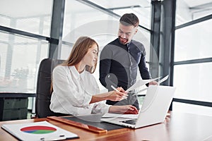 Woman and man in formal clothes working together indoors in the office by table