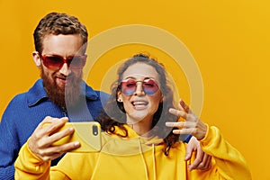 Woman and man funny couple with phones hand social networking and communication crooked do selfies smile fun, on yellow