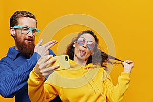 Woman and man funny couple with phones hand social networking and communication crooked do selfies smile fun, on yellow