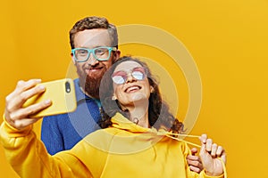 Woman and man funny couple with phones hand social networking and communication crooked do selfies smile fun, on yellow