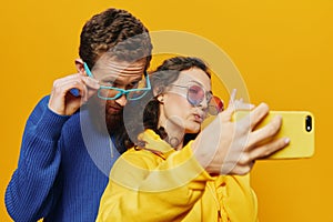 Woman and man funny couple with phones hand social networking and communication crooked do selfies smile fun, on yellow