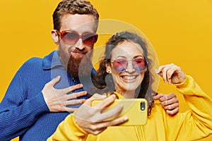 Woman and man funny couple with phones hand social networking and communication crooked do selfies smile fun, on yellow