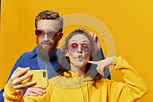 Woman and man funny couple with phones hand social networking and communication crooked do selfies smile fun, on yellow