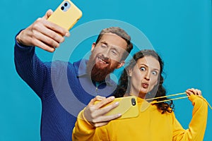 Woman and man funny couple with phones in hand taking selfies crooked smile fun, on blue background. The concept of real