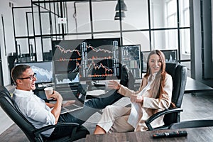 Woman and man have conversation. Team of stockbrokers works in modern office with many display screens