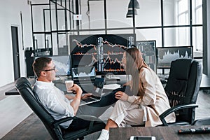 Woman and man have conversation. Team of stockbrokers works in modern office with many display screens