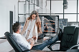 Woman and man have conversation. Team of stockbrokers works in modern office with many display screens photo