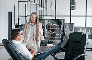 Woman and man have conversation. Team of stockbrokers works in modern office with many display screens
