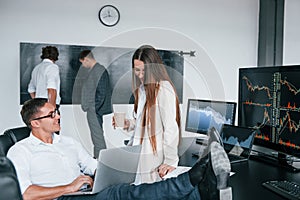 Woman and man have conversation. Team of stockbrokers works in modern office with many display screens