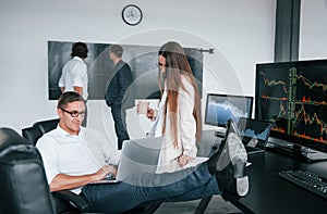 Woman and man have conversation. Team of stockbrokers works in modern office with many display screens