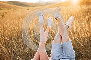 Woman and man having fun outdoors. Loving hipster couple are lying in the grass and lifting their legs in sneakers up in