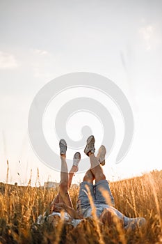 Woman and man having fun outdoors. Loving hipster couple are lying in the grass and lifting their legs in sneakers up in