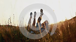 Woman and man having fun outdoors. Loving hipster couple are lying in the grass and lifting their legs in sneakers up in