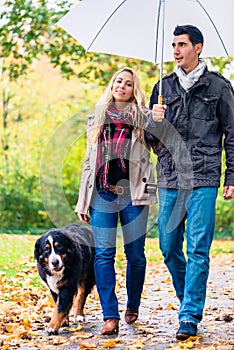 Woman and man having walk with dog in autumn rain