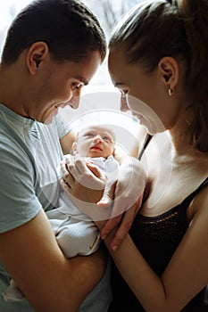 Woman and man holding on hands a newborn. On the background window. Mom, dad and baby. Portrait of young family. Happy family life