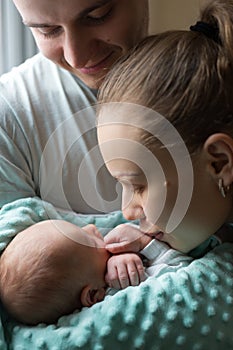 Woman and man holding on hands a newborn. Mom, dad and baby. Mother kissing her son. Happy family life. Man was born