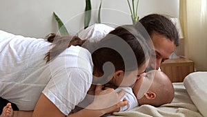 Woman And Man Holding Newborn. Mom, Dad And Baby On Bed. Close-up. Portrait of Young Smiling Family With Newborn On