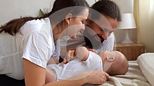 Woman And Man Holding Newborn. Mom, Dad And Baby On Bed. Close-up. Portrait of Young Smiling Family With Newborn On