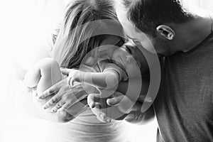 Woman and man holding a newborn. Mom, dad and baby. Close-up. Portrait of young smiling parents kissing their baby