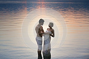 Woman and man hugged in water at sunset