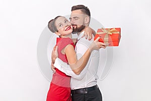 Woman and man hugging each other, female holding red present box, husband kissing his wife.