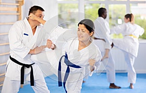 Woman and man in kimono sparring in gym during karate training