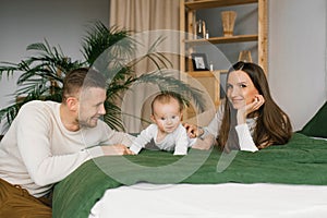 Woman and a man are lying on a bed with their baby son. Mom, Dad and baby, happy family at home