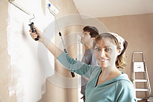 Woman And Man Painting Wall With Paint Rollers