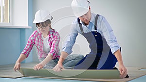 woman and man in protective helmets check locks of laminate for laying on floor during renovation and reconstruction of