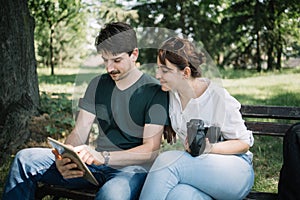 Woman and man sitting on bench and looking at tablet`s display