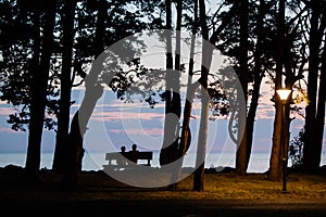 A woman and a man sitting on a bench and meeting the sunset on the beach