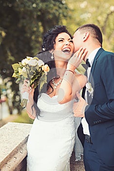 Woman and man smile on wedding day. Groom kiss happy bride with bouquet. Wedding couple in love. Newlywed couple on