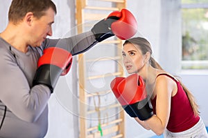 Woman and man in sportswear are engaged in boxing sparring in gym