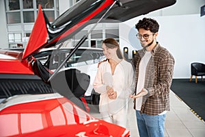 Woman and man standing near modern red automobile buying new car in dealership