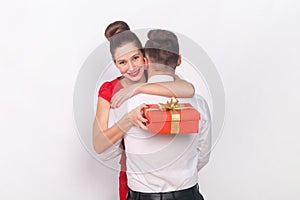 Woman and man standing together, guy posing backwards, his wife hugging him and holding present box.