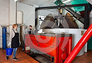 Woman and man supervising milling olives in crusher machine