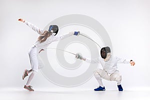 The woman and man wearing fencing suit practicing with sword against gray