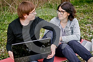 A woman and a man work on a laptop remotely against a background of a blooming garden and green grass. A happy family