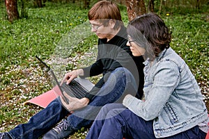 A woman and a man work on a laptop remotely against a background of a blooming garden and green grass. A happy family